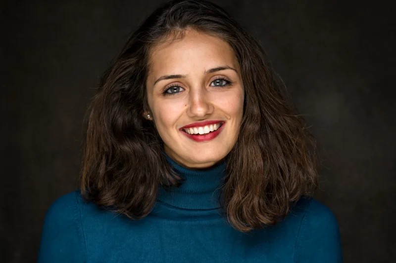 Portret van een glimlachende vrouw in een blauwe trui tegen een donkere achtergrond.